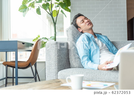 自宅 リビングルームで書類を片手に悩む若い男性 自宅 リビングルームで書類を片手に悩む若い男性 62372053
