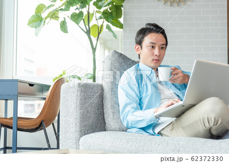 自宅のリビングでノートパソコンで仕事をする若い実業家 62372330