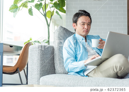 自宅のリビングでノートパソコンで仕事をする若い実業家 自宅のリビングでノートパソコンで仕事をする若い実業家 62372365