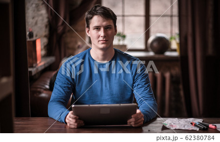 Serious Young Man Uses His Tablet While Working In Cozy Coworking Space. 62380784