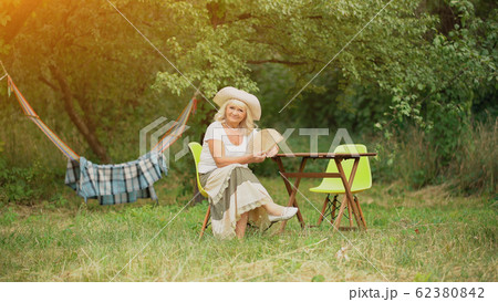 Old Lady sits in garden across hamack. Old Lady sits in garden across hamack. 62380842