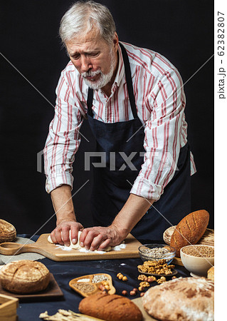 Mature bearded baker man kneading dough for bread on table Mature bearded baker man kneading dough for bread on table 62382807