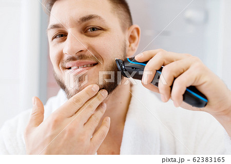 Man shaves his beard with an electric razor Man shaves his beard with an electric razor 62383165