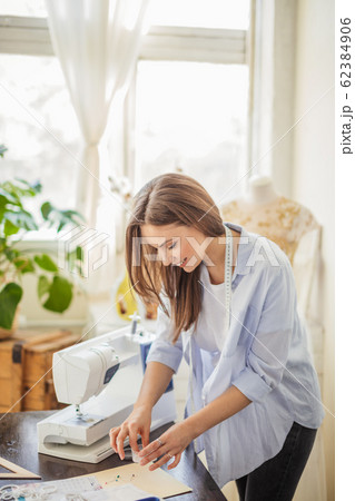 Beautiful seamstress is working with a wedding dress model in her studio 62384906