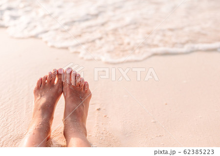 Woman's feet on the white sand beach in shallow water 62385223