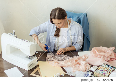 Beautiful focused young fashion designer cutting pink lace fabric in workshop Beautiful focused young fashion designer cutting pink lace fabric in workshop 62385470