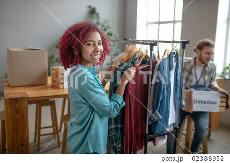 Young girl near rack with clothes man with donation box. 62388952