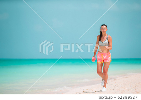 Fit young woman doing exercises on tropical white beach in her sportswear Fit young woman doing exercises on tropical white beach in her sportswear 62389527