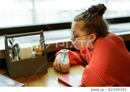 Girl teenager sitting in a cafe at a table waiting and drinking Girl teenager sitting in a cafe at a table waiting and drinking 62390392
