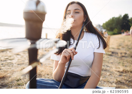 Woman holding pipe smoking shisha alone outside 62390595