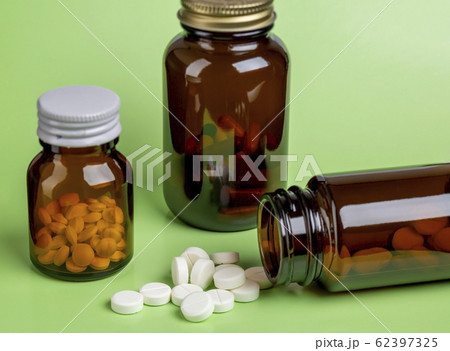 three glass bottles of pills on a green background of scattered white pills 62397325