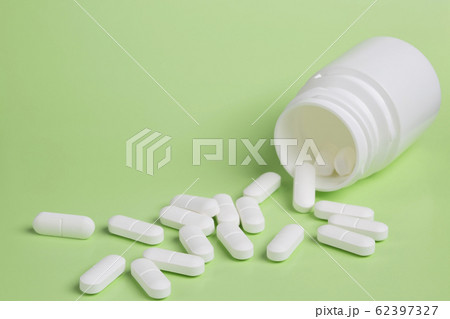 Plastic white bottles of pills on a green background of scattered white pills 62397327