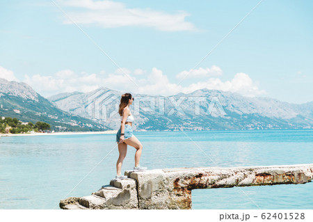 time to travel. beautiful woman in white topic and jeans shorts alone on seaside looking to the blue ocean and enjoying the view time to travel. beautiful woman in white topic and jeans shorts alone on seaside looking to the blue ocean and enjoying the view 62401528
