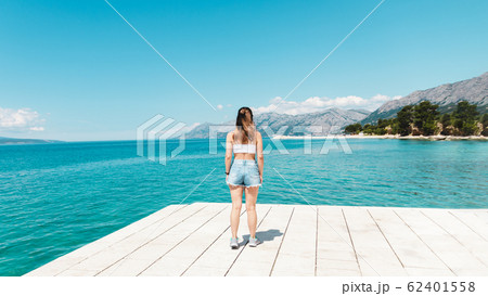 time to travel. beautiful woman in white topic and jeans shorts alone on seaside looking to the blue ocean and enjoying the view 62401558