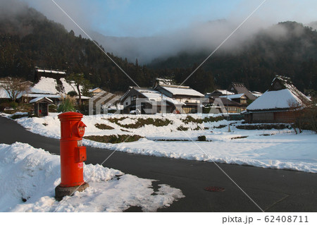 暖冬のかやぶきの里に射す朝日　山には霧　京都府美山町 62408711