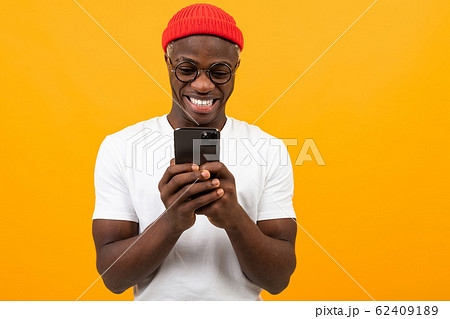 american man smiling holding a smartphone in his hands on a yellow background with copy space 62409189