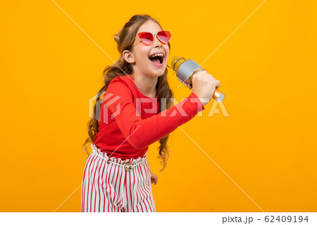 young singer with a microphone in her hands on a yellow studio background with copy space 62409194