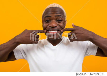 closeup portrait of a smiling handsome black blond african man with grimace over orange background closeup portrait of a smiling handsome black blond african man with grimace over orange background 62409195