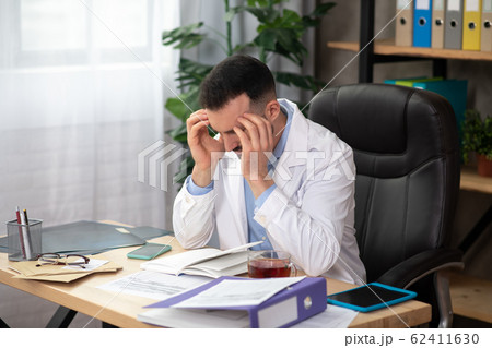 Dark-haired bearded doctor in a white robe suffering from headache Dark-haired bearded doctor in a white robe suffering from headache 62411630