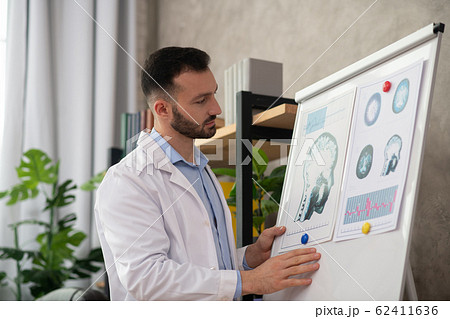 Young bearded doctor in a white robe looking involved working with drawings 62411636