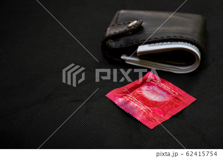 Closeup woman hand holding black Leather Wallet with a red condom at the black background Closeup woman hand holding black Leather Wallet with a red condom at the black background 62415754