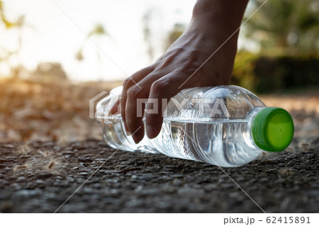 Close up Hand picking up clear plastic bottle water drink with a green cap on the road in the park at blurred background Close up Hand picking up clear plastic bottle water drink with a green cap on the road in the park at blurred background 62415891