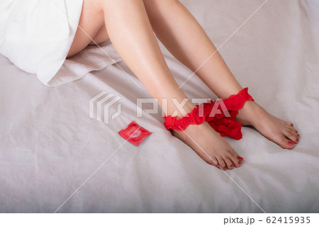 Red condoms and beautiful leg sexy woman reclines on the bed with red g-string between feet 62415935