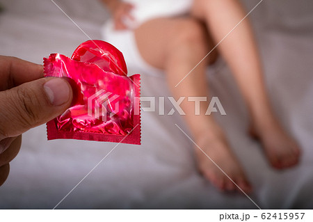 Man showing red condom at the beautiful woman with towel lies in bed 62415957