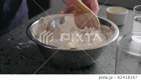 man mixing dry ingredients with flour in steel bowl on concrete countertop 62418167