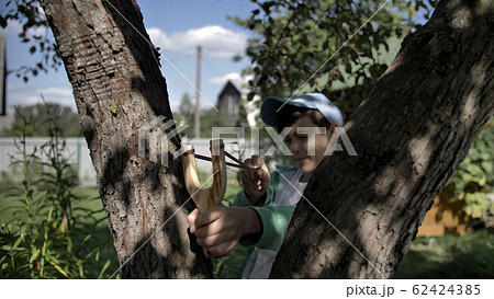 boy hides behind a tree and aims at someone with a slingshot 62424385