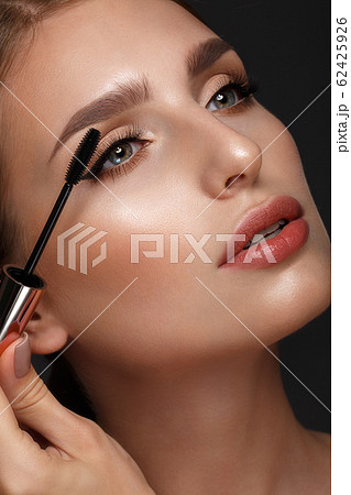 Beautiful girl with sexy lips and classic makeup with cosmetic mascara brush in hand. Beauty face. Beautiful girl with sexy lips and classic makeup with cosmetic mascara brush in hand. Beauty face. 62425926