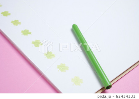 ピンクのバック紙の上の黄緑色の色鉛筆と四葉のクローバーが書かれたスケッチブック 62434333