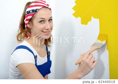 pretty young woman painting the wall yellow color pretty young woman painting the wall yellow color 62440019