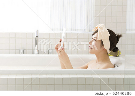 バスルームで防水ケースにスマホを入れて観覧する若い女性 62440286