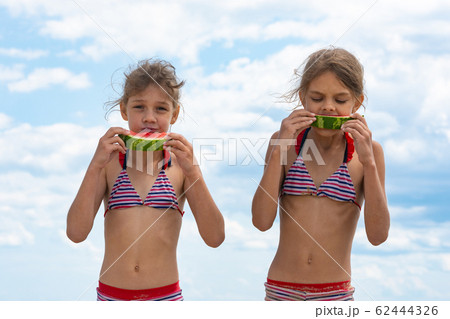 Two girls eat watermelon on the beach against the 62444326