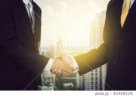 Two cheerful businessman shaking hands with city background, anonymous face Two cheerful businessman shaking hands with city background, anonymous face 62448129