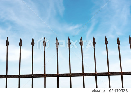 Wrought iron fence with sharp points on blue sky with clouds Wrought iron fence with sharp points on blue sky with clouds 62450528