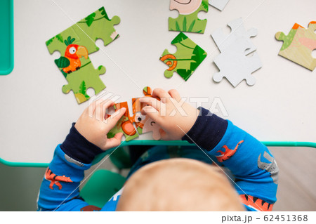 Baby boy solving jigsaw puzzle on the desk Baby boy solving jigsaw puzzle on the desk 62451368