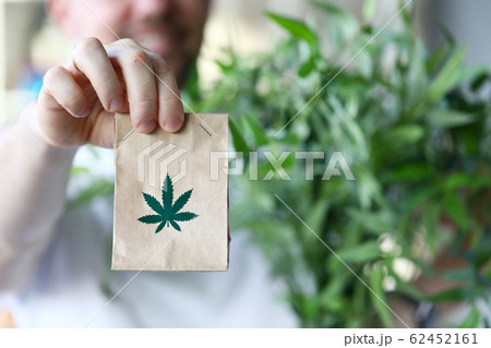 Male hand hold paper packet with marijuana symbol closeup background Male hand hold paper packet with marijuana symbol closeup background 62452161