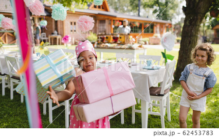 Portrait of small girl with presents outdoors in garden in summer. 62453783