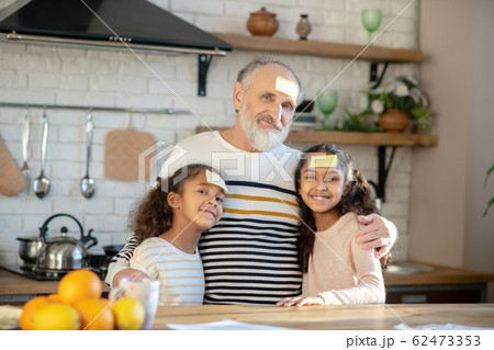 Bearded grey-haired man hugging his dark-skinned granddaughters 62473353