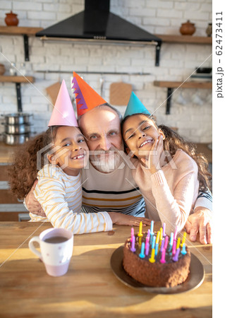 Bearded grey-haired man and his dark-skinned girls celebrating bithday Bearded grey-haired man and his dark-skinned girls celebrating bithday 62473411