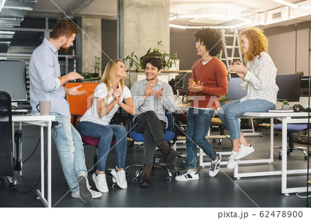 Cheerful young coworkers welcoming new colleague in modern coworking space 62478900