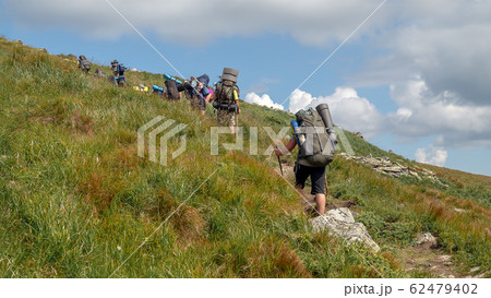 Tourists with hiking backpacks walk along a Tourists with hiking backpacks walk along a 62479402