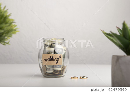 Savings in glass bank jar and Wedding Rings over gray 62479540