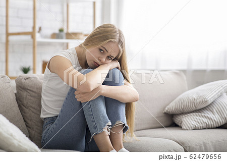 Lonely sad girl sitting on couch at home alone Lonely sad girl sitting on couch at home alone 62479656