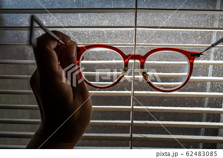 Woman's hand holding shortsighted or nearsighted eyeglasses with Dust blinds inside a window, Dust and Dirty mosquito wire screen window, Light & Shadow shot, Close up shot, Selective focus 62483085