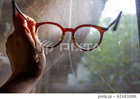 Woman's wet hand holding shortsighted or nearsighted eyeglasses with Dust and Dirty mosquito wire screen window, Close up shot, Selective focus 62483086
