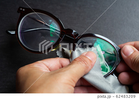 Woman's hands cleaning shortsighted or nearsighted eyeglasses by microfibre cleaning cloths, On black background, Close up & Macro shot, Selective focus, Optical concept Woman's hands cleaning shortsighted or nearsighted eyeglasses by microfibre cleaning cloths, On black background, Close up & Macro shot, Selective focus, Optical concept 62483209