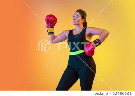 Young caucasian plus size female model's training on gradient orange background 62486631